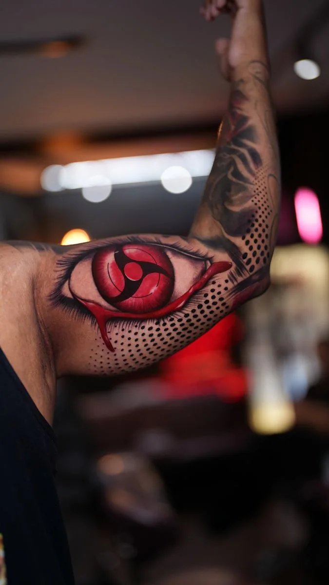 Tatuaje anime a color: ojo rojo con lágrima de sangre y puntillismo, en el brazo · Wilson Escobar, tatuador en Miami