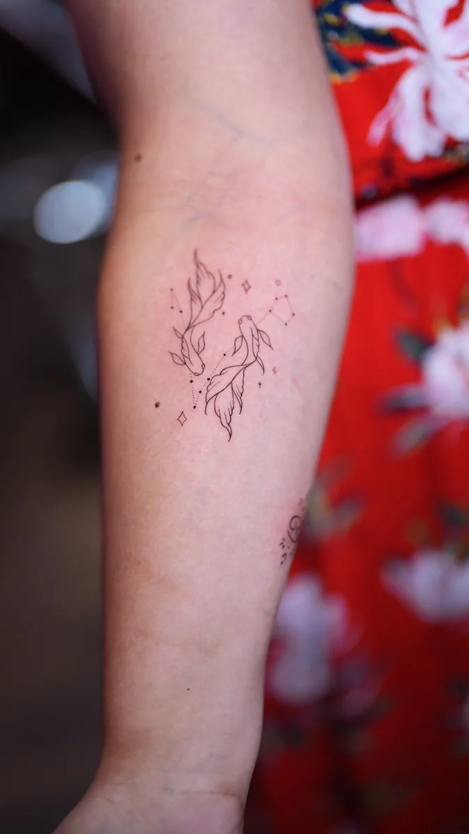 Tatuaje fine line: dos peces con estrellas, en el antebrazo · Wilson Escobar, tatuador en Miami
