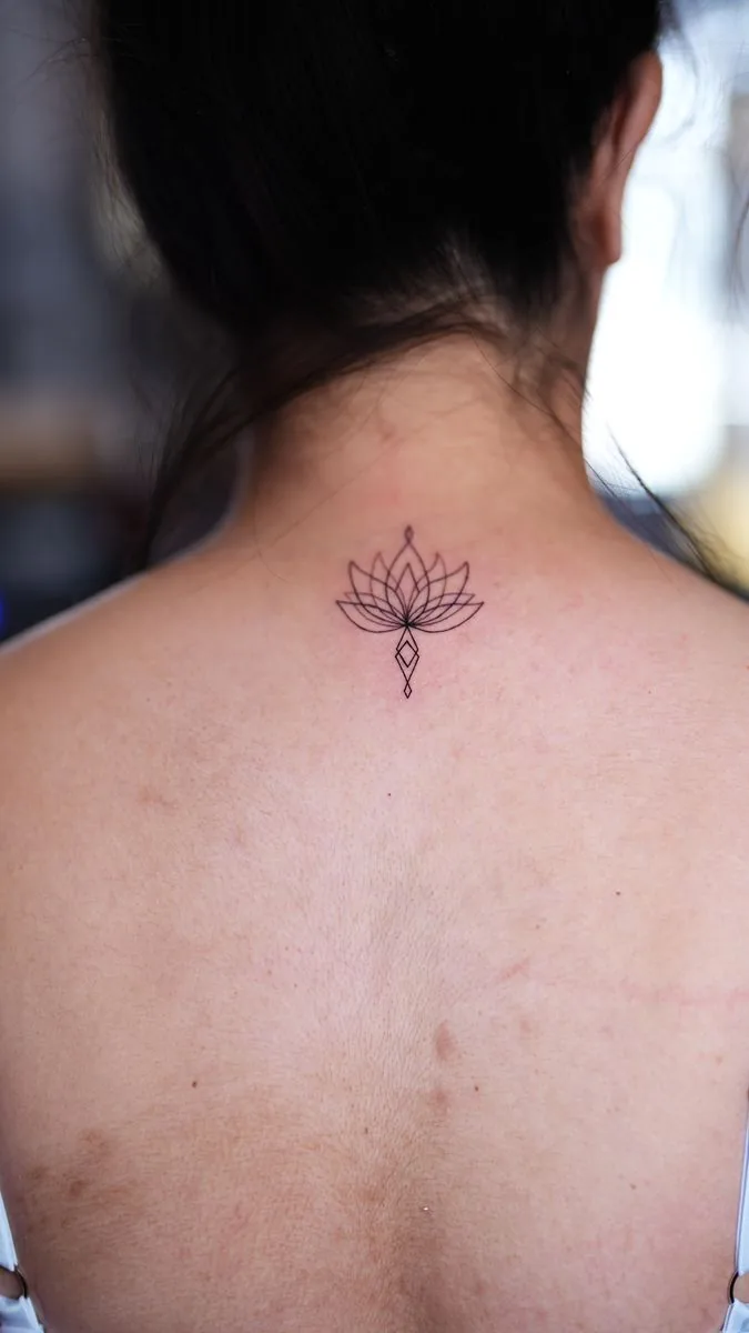 Tatuaje fine line: flor de loto en la espalda, debajo de la nuca · Wilson Escobar, tatuador en Miami