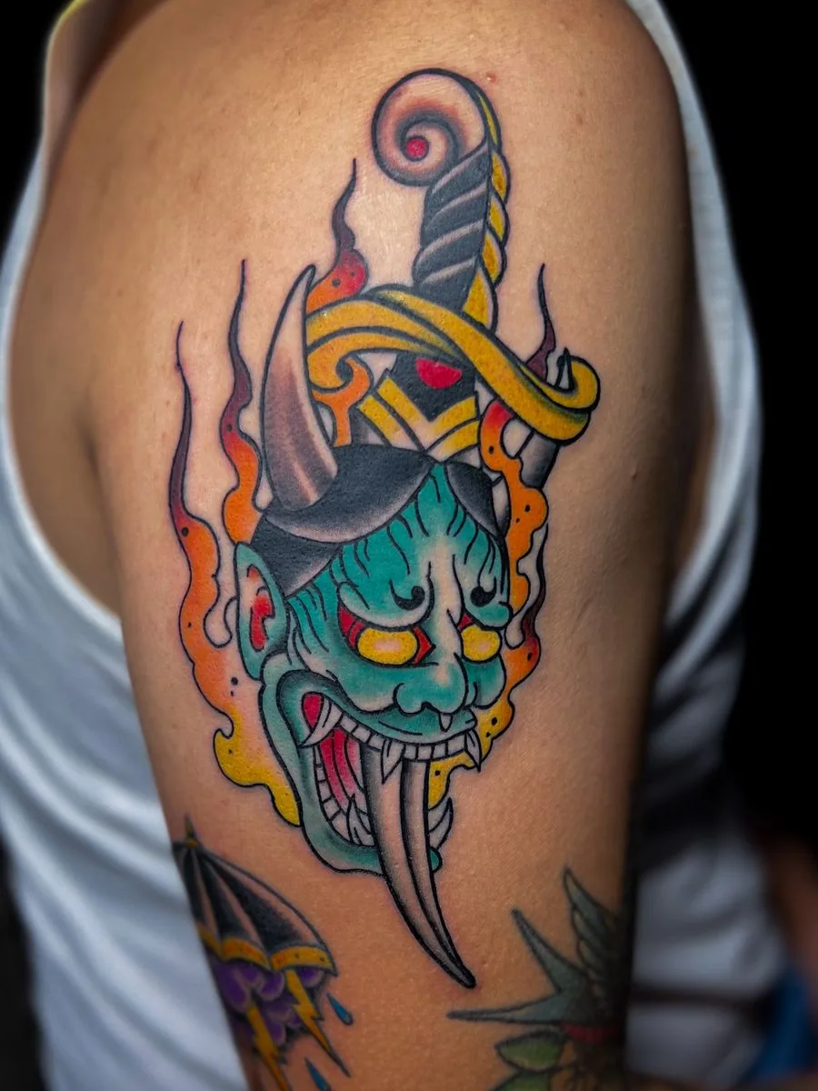 Tatuaje a color: máscara japonesa con daga y llamas, en el brazo · Wilson Escobar, tatuador en Miami