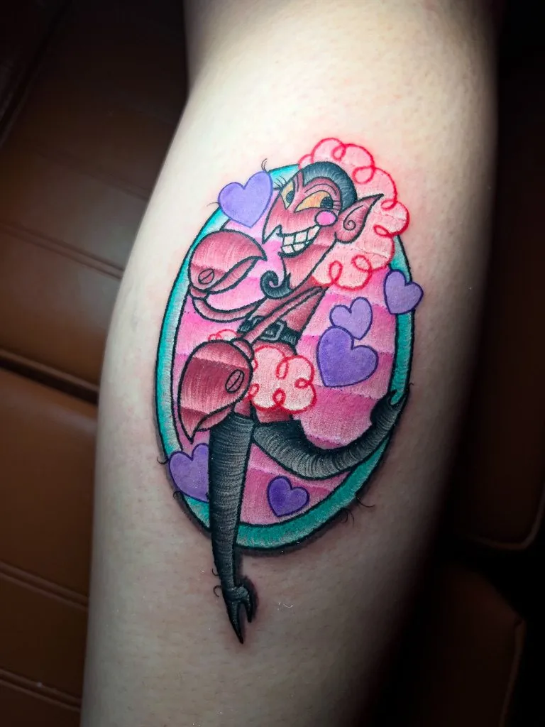 Tatuaje a color estilo parche: personaje de caricatura con corazones en un óvalo con borde bordado, en la pierna · Wilson Escobar, tatuador en Miami