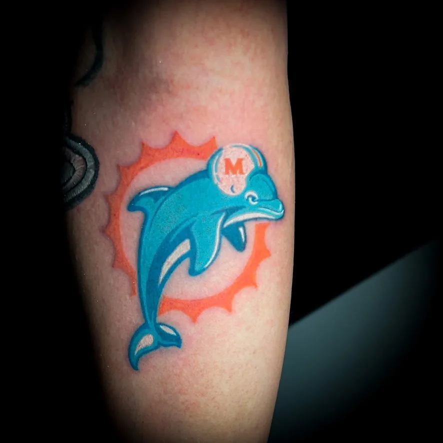Tatuaje a color: delfín frente a un sol naranja · Wilson Escobar, tatuador en Miami